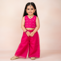 Young girl in a pink traditional outfit with a polka dot top and wide-leg pants on a beige background