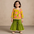 Young girl wearing a yellow floral top and green pants against a beige background